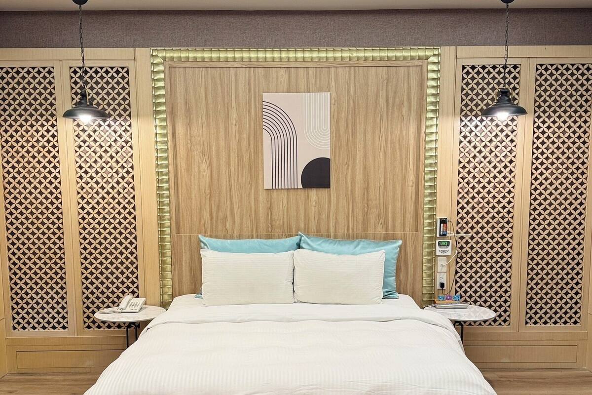 Un dormitorio moderno con una cama grande, dos mesitas de noche, una obra de arte en la pared y un diseño de pared estampado.