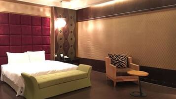 Una habitación de hotel moderna con una cama grande, un sofá verde, un sillón de madera con un cojín estampado de cebra y una pequeña mesa redonda.