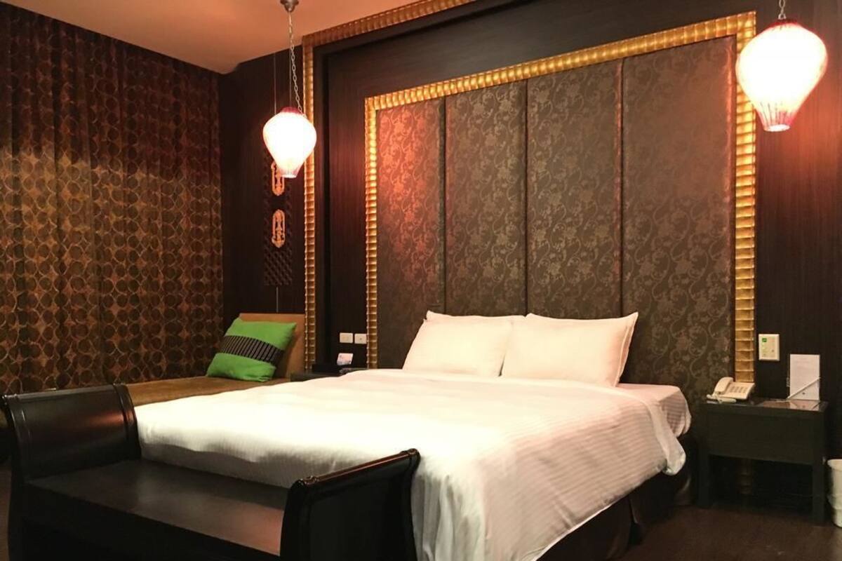 Habitación de hotel con una cama grande, un banco, una mesita de noche y una pared con papel tapiz estampado.