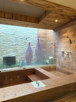 Un baño moderno con pared de piedra, cerramiento de vidrio y bañera empotrada.