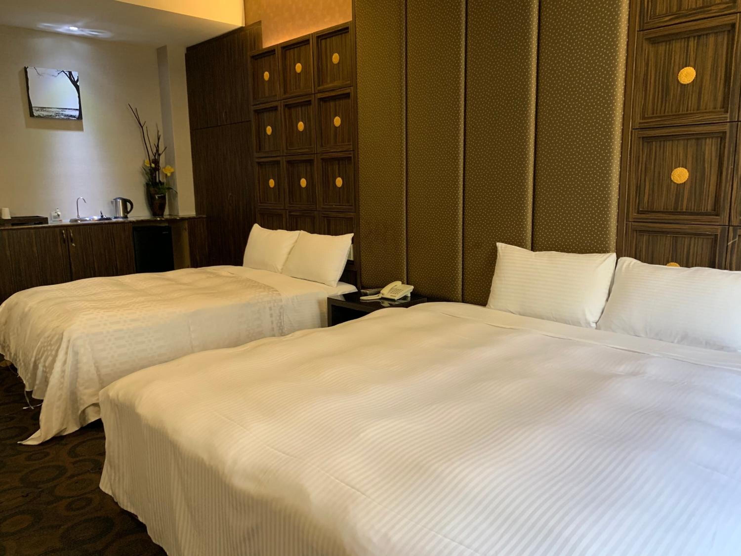 A hotel room with two beds, a small desk with a phone, and a wall-mounted TV.