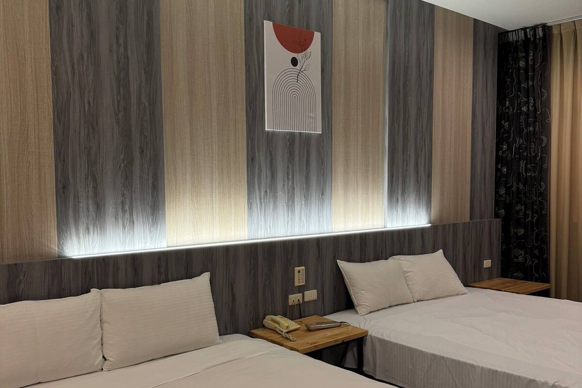 Habitación de hotel con dos camas, cabecera de madera, una obra de arte colgada en la pared y una mesita de noche con teléfono y control remoto.