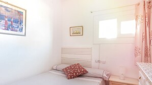 Une petite chambre à coucher, bien rangée, avec un lit simple, une table de chevet, une commode et une fenêtre avec des rideaux.