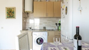 Une cuisine avec des meubles en bois, un lave-linge, un évier et une table à manger sur laquelle se trouvent une bouteille de vin et des verres.