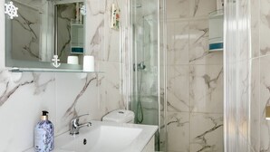 Une salle de bain moderne avec un pare-baignoire en marbre, une douche en verre et un lavabo blanc doté d’un distributeur de savon.