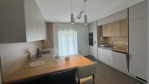 Ett modernt kök med ett matbord i trä, två hängande lampor och ett fönster med tunna, genomskinliga gardiner.