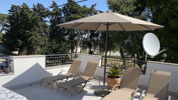 En takterrass med fyra beige solstolar, ett stort beige parasoll och en satellitmottagare.