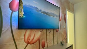 En platt-TV som är monterad på väggen ovanför en väggmålning med blommotiv, ett vitt skåp under TV:n och en fjärrkontroll som ligger på skåpet.