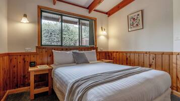 A bedroom with a wooden headboard, a large bed with a striped duvet, two bedside tables, and a window with a view of trees.