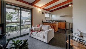 Un salon confortable avec un canapé, une table basse en verre et un téléviseur. Il y a un balcon avec vue sur les arbres et les montagnes. La cuisine est équipée de meubles en bois et d’un four à micro-ondes.