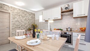A modern kitchen with white cabinets, a wooden dining table set for two, and a brick-patterned wall. - 2 bedroom pet friendly home in Skrljevo (Skrljevo)