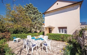 A patio with a table set for four, surrounded by white chairs, in front of a building with a beige exterior and a small window.