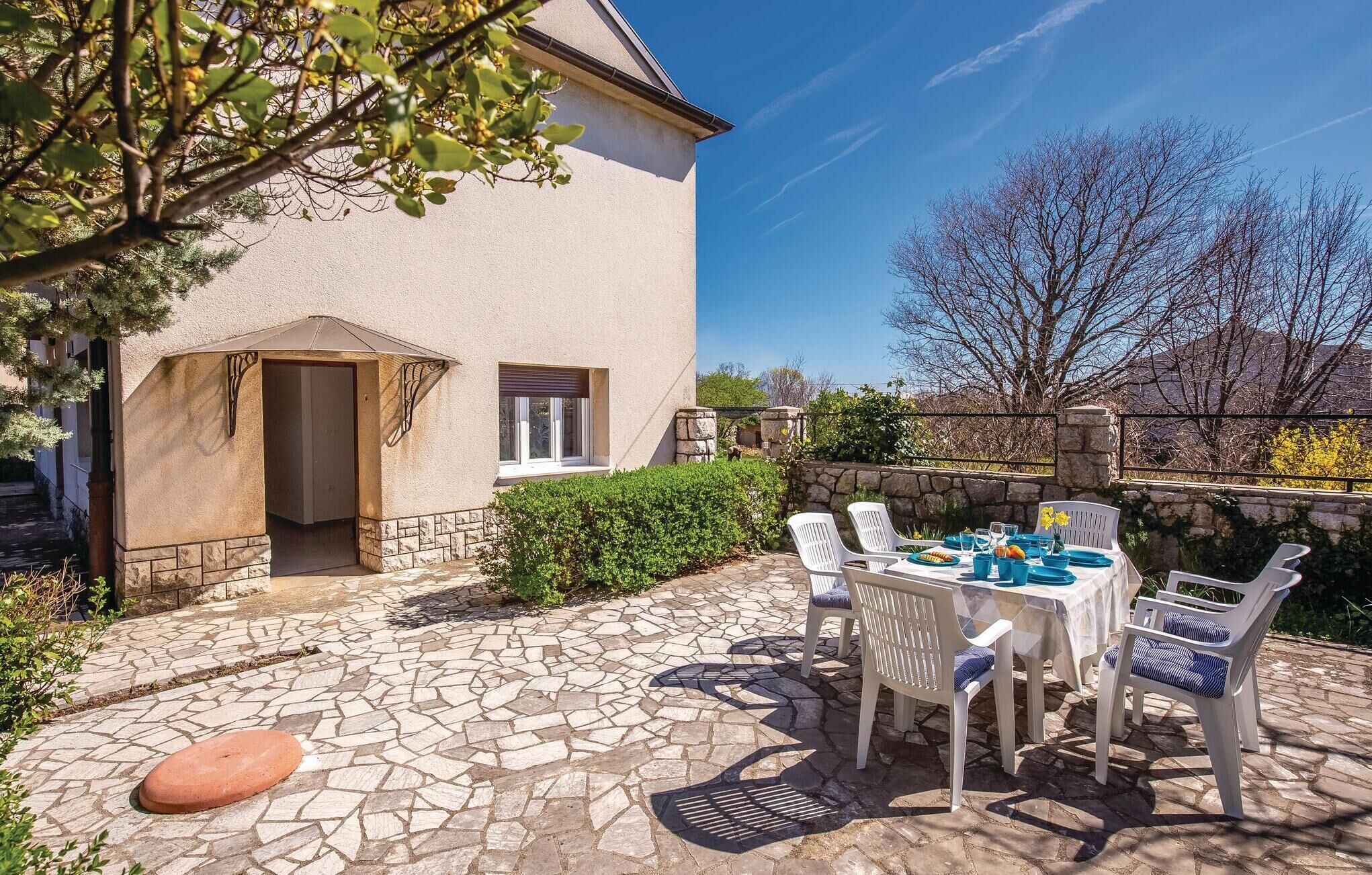 A stone patio with a table set for dining, surrounded by white chairs with blue cushions.