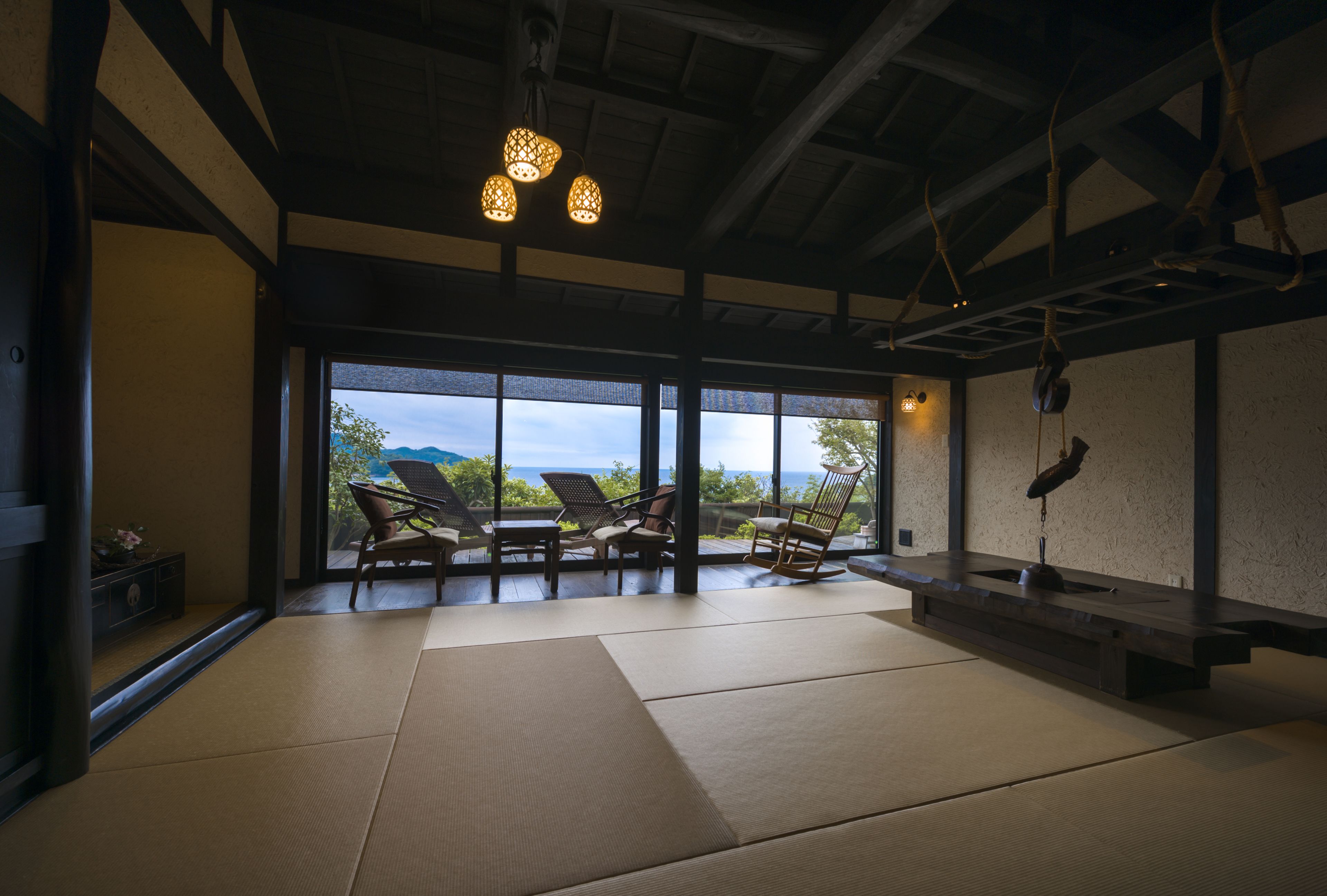 A room with tatami mats, wooden furniture, and a view of the sea.