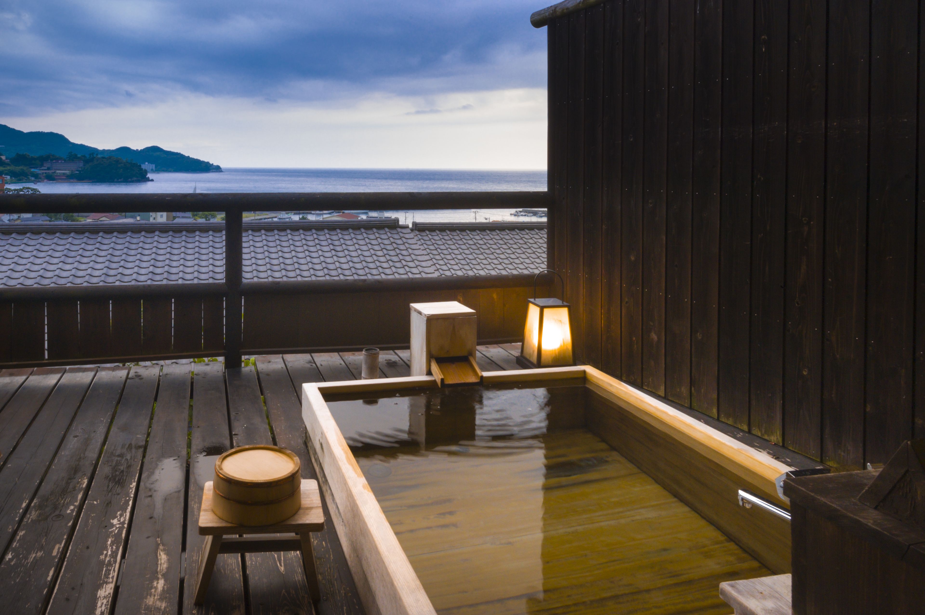 A wooden deck with a hot spring bath, a wooden stool, and a lantern.