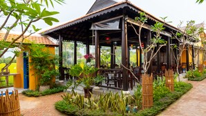 A covered outdoor seating area with wooden furniture and potted plants. - Chez Mimosa Hoi An - Rice Field Retreat (Da Nang)