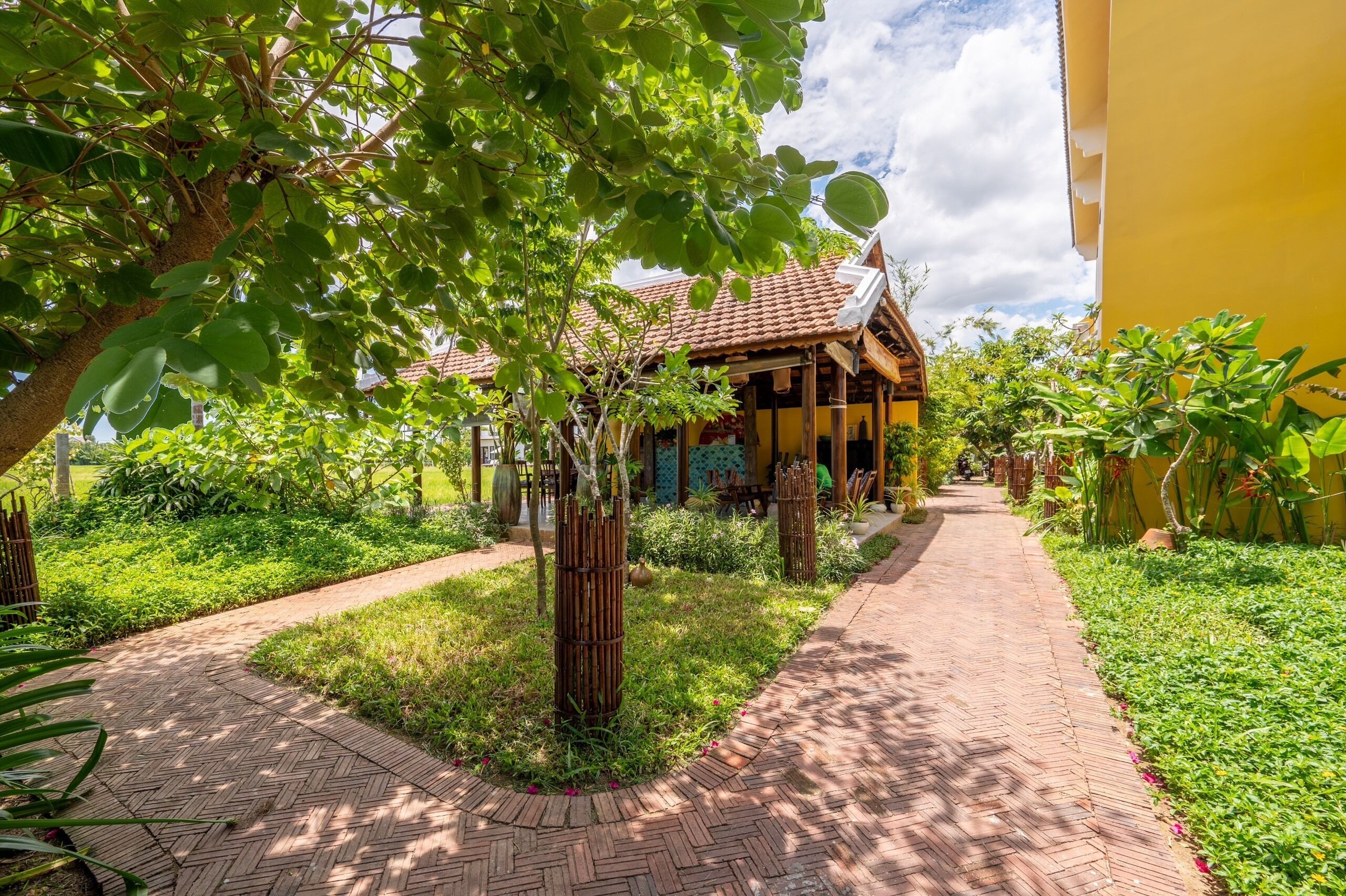 A pathway leading to a traditional building with a tiled roof, surrounded by lush greenery and a well-maintained garden.