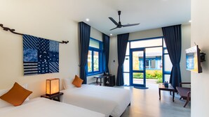 A hotel room with two beds, a ceiling fan, a desk with a chair, and a view of the outside. - Chez Mimosa Hoi An - Rice Field Retreat (Da Nang)