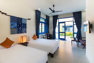 Habitación de hotel con dos camas, un ventilador de techo, un escritorio con una silla y vistas al exterior.