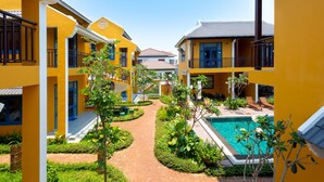 A courtyard with a swimming pool, surrounded by yellow buildings with balconies and a clear sky. - Chez Mimosa Hoi An - Rice Field Retreat (Da Nang)