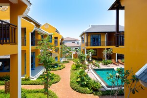 Un patio con piscina, rodeado de edificios amarillos con balcones y cielo despejado.