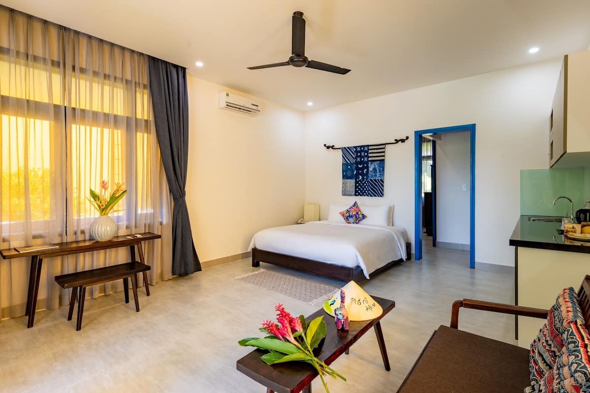 A hotel room with a bed, desk, and kitchenette.