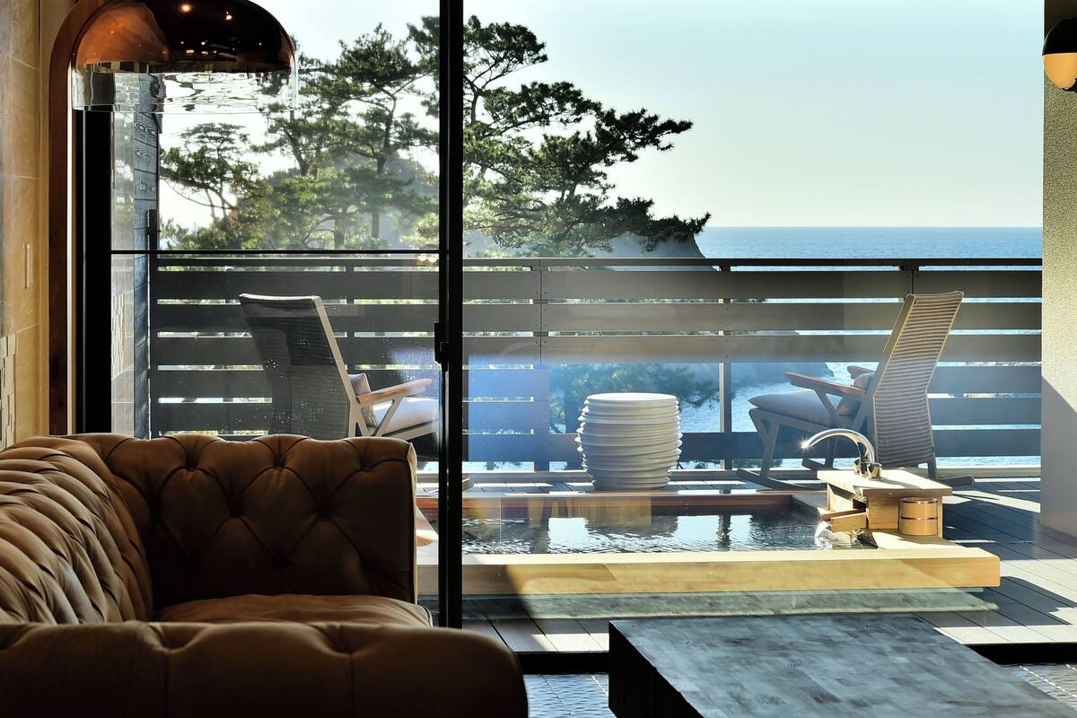 A modern lounge area with a cushioned seating arrangement, a small water feature, and a view of the ocean.