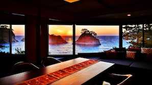 A dining area with a view of the ocean and sunset through large windows. - Mayu Futahari (Nishiizu)
