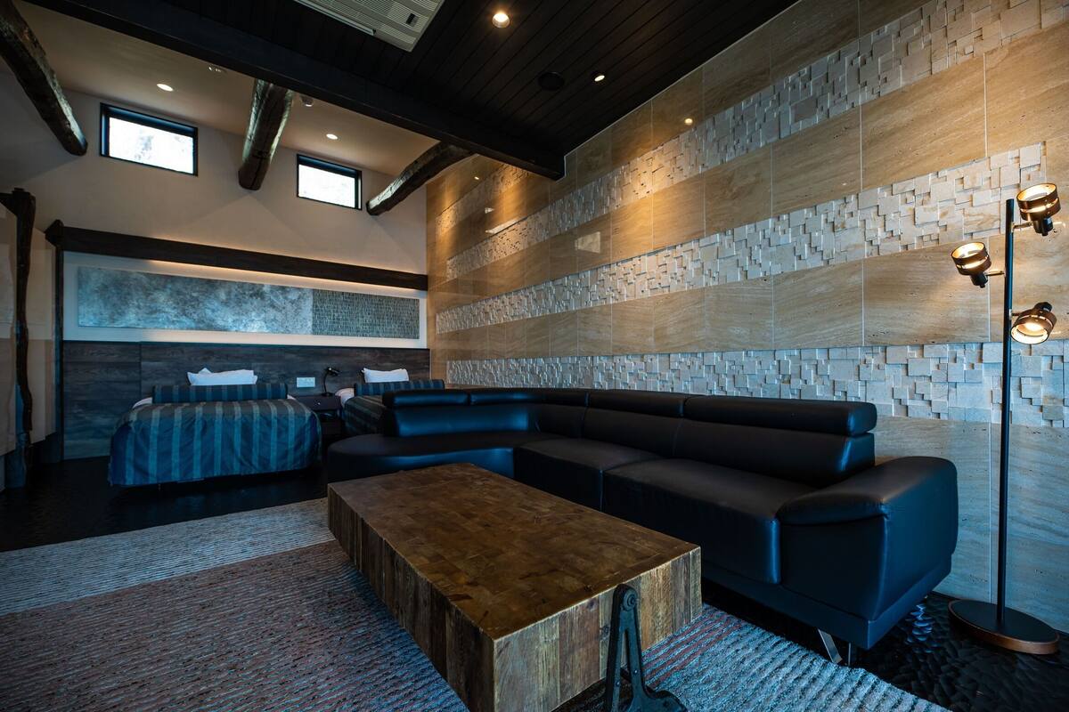 A modern living room with a sectional sofa, a wooden coffee table, and a stone-patterned wall.