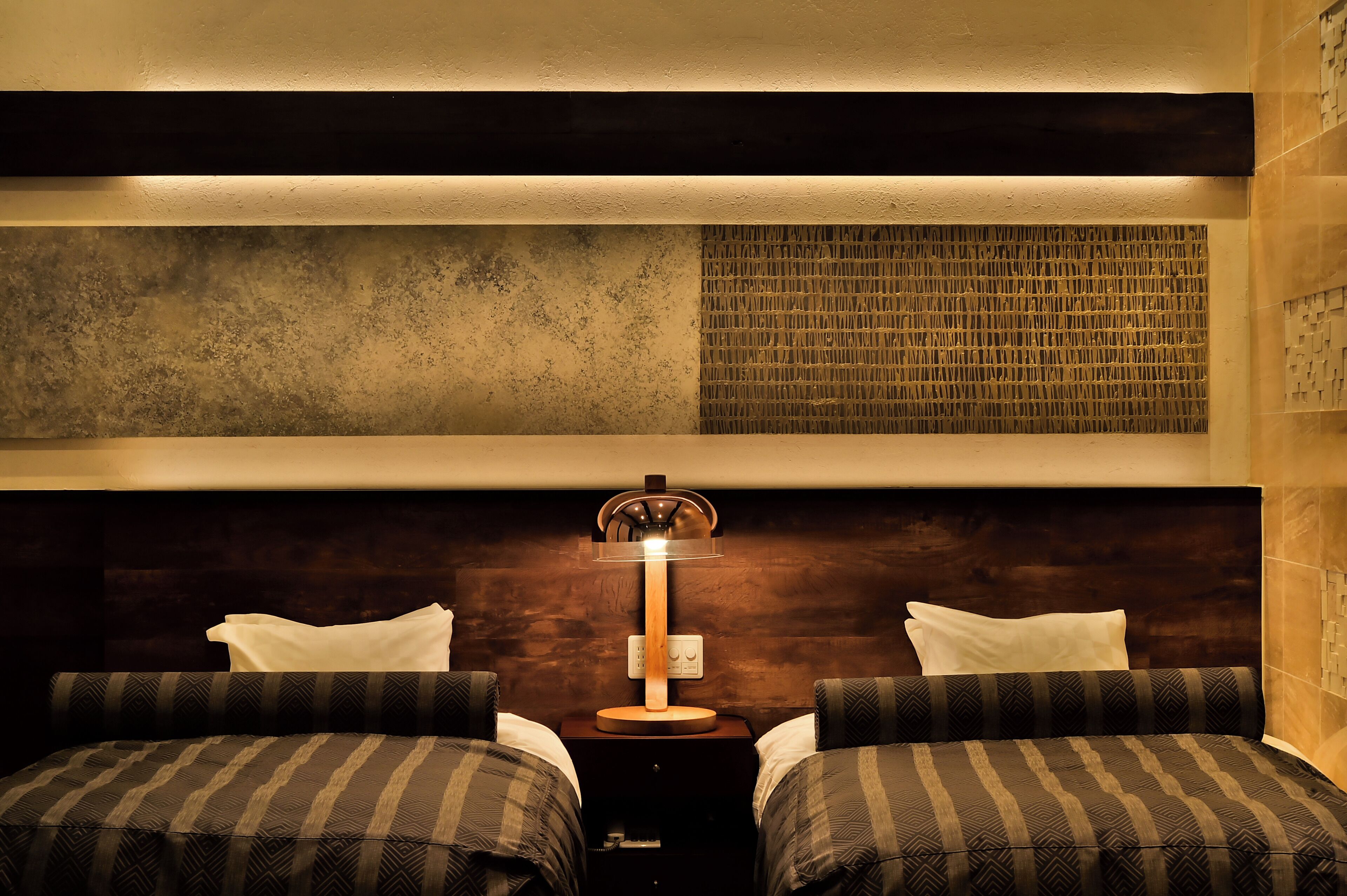 Een hotelkamer met twee bedden, een wandlamp en een wanddecoratie met reliëf.
