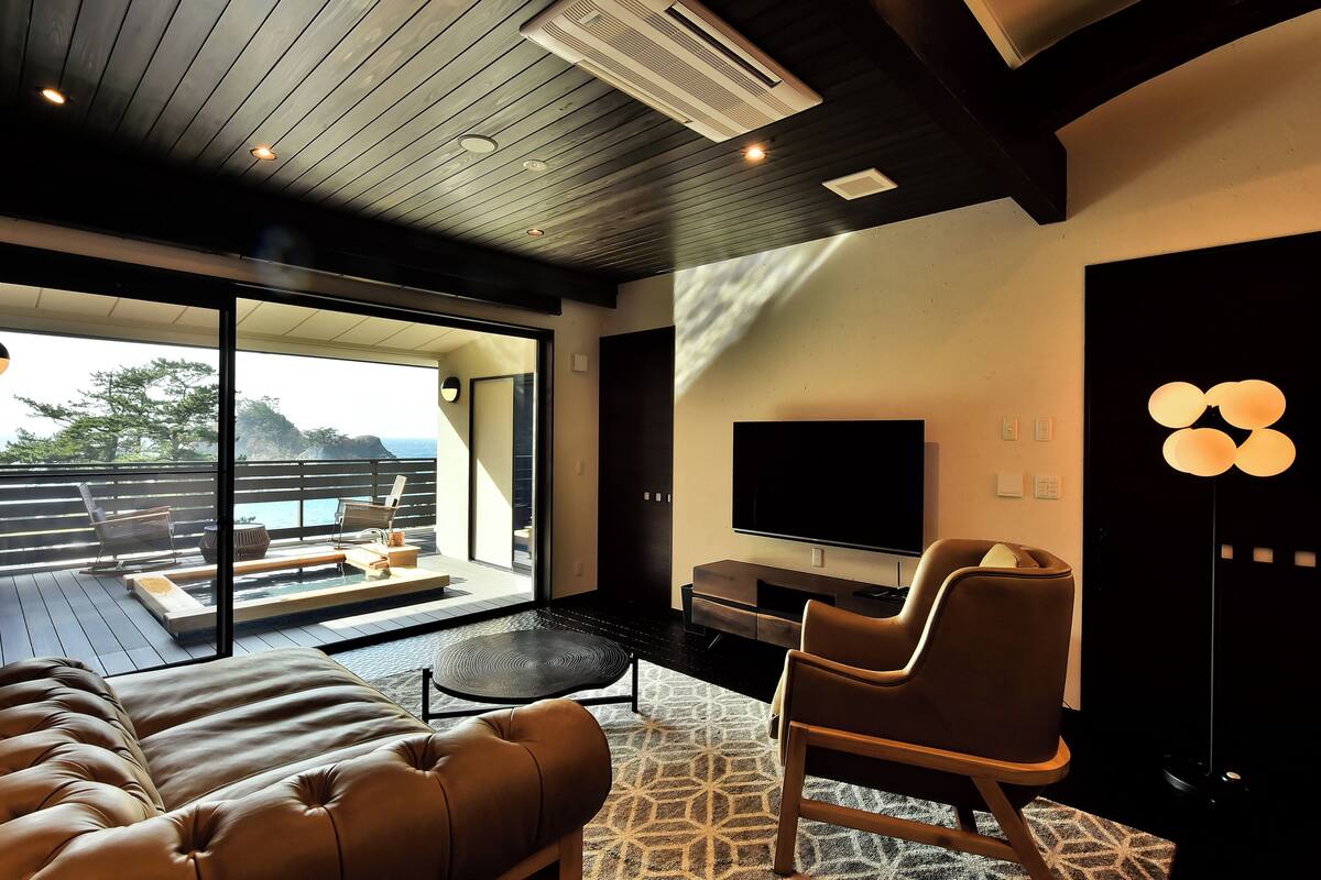 A modern living room with a large flat-screen TV, comfortable seating, and a view of the outdoors.