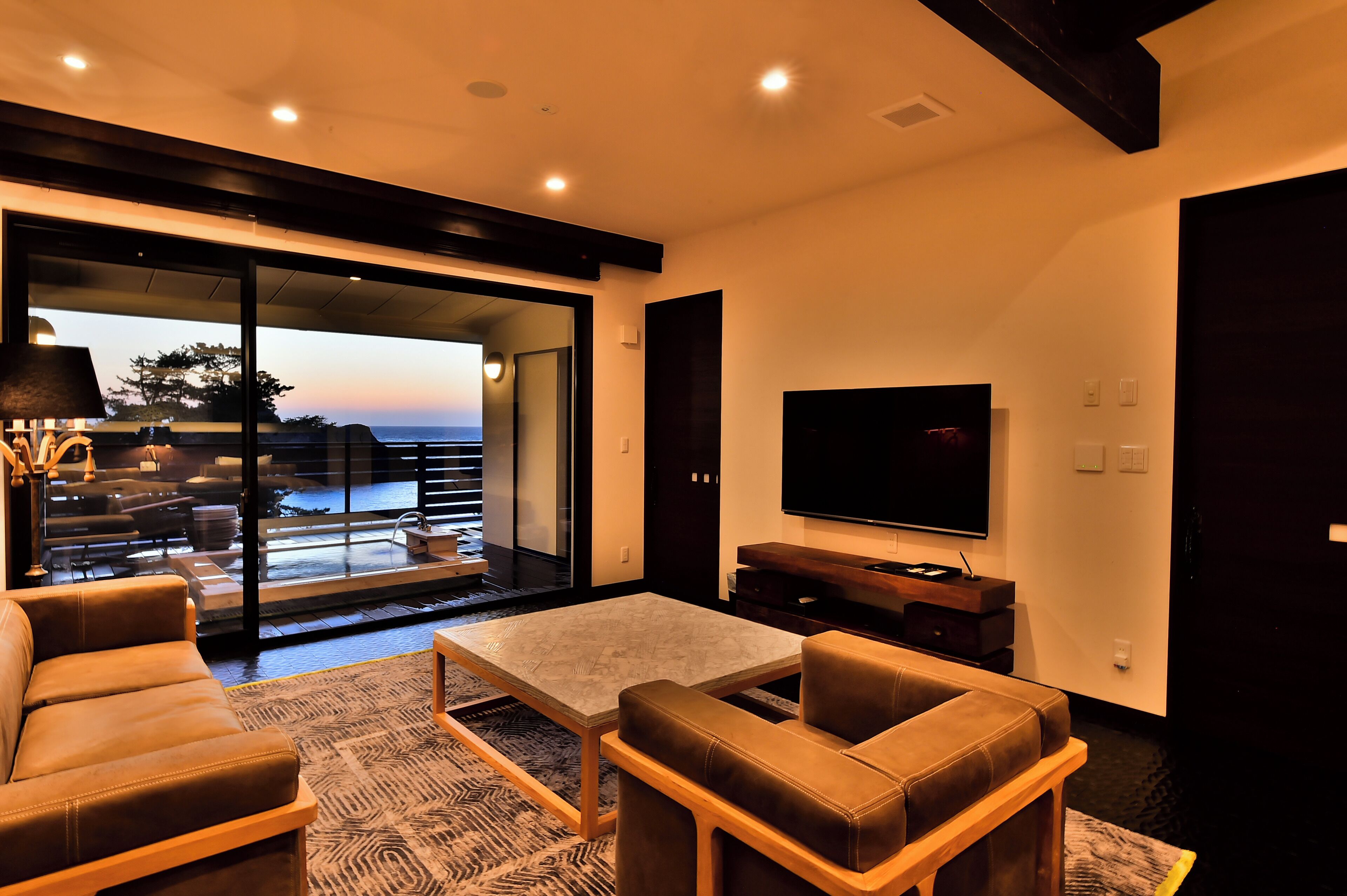 A modern living room with a large TV, comfortable seating, and a view of the outdoors.