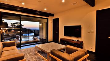 A modern living room with a large TV, comfortable seating, and a view of the outdoors.