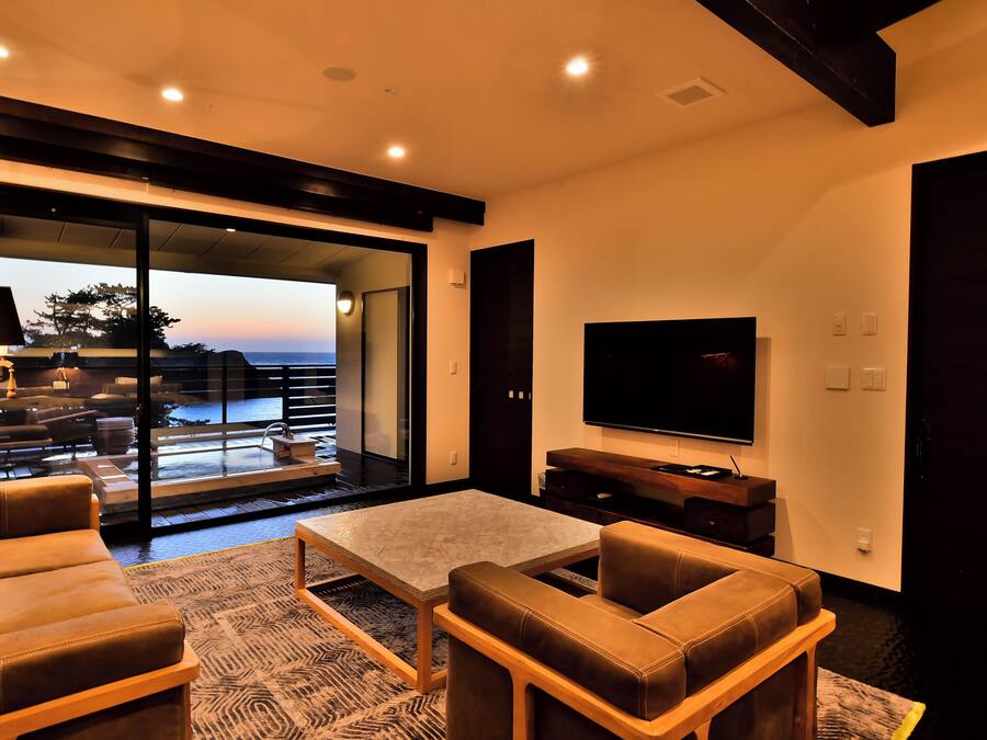 A modern living room with a large TV, comfortable seating, and a view of the outdoors.