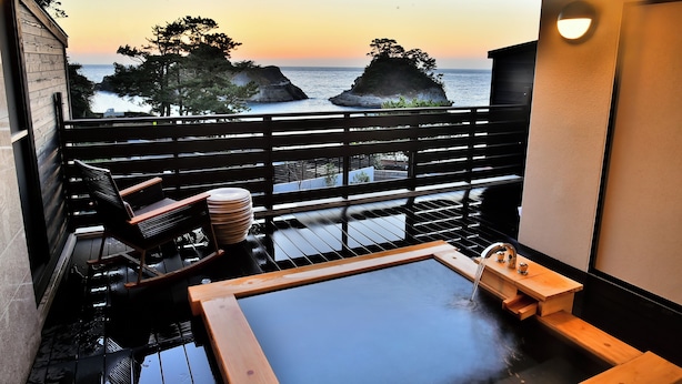 A balcony with a hot tub, wooden furniture, and a view of the sea at sunset. - Mayu Futahari (Nishiizu)