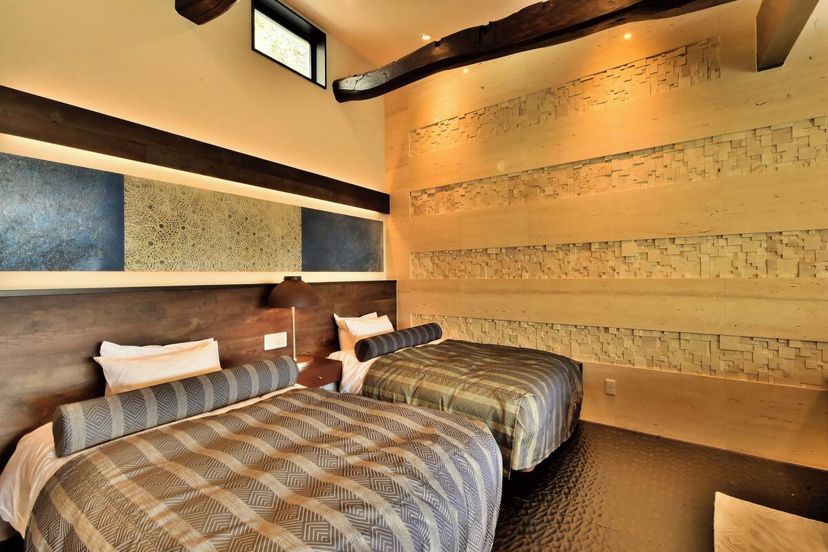 A hotel room with two beds, a wooden headboard, a textured wall, and a small window.