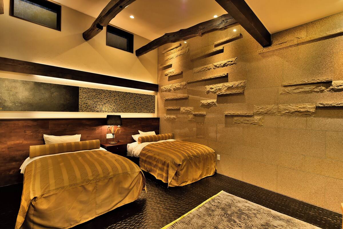 A hotel room with two beds, a stone wall, and a wooden ceiling beam.