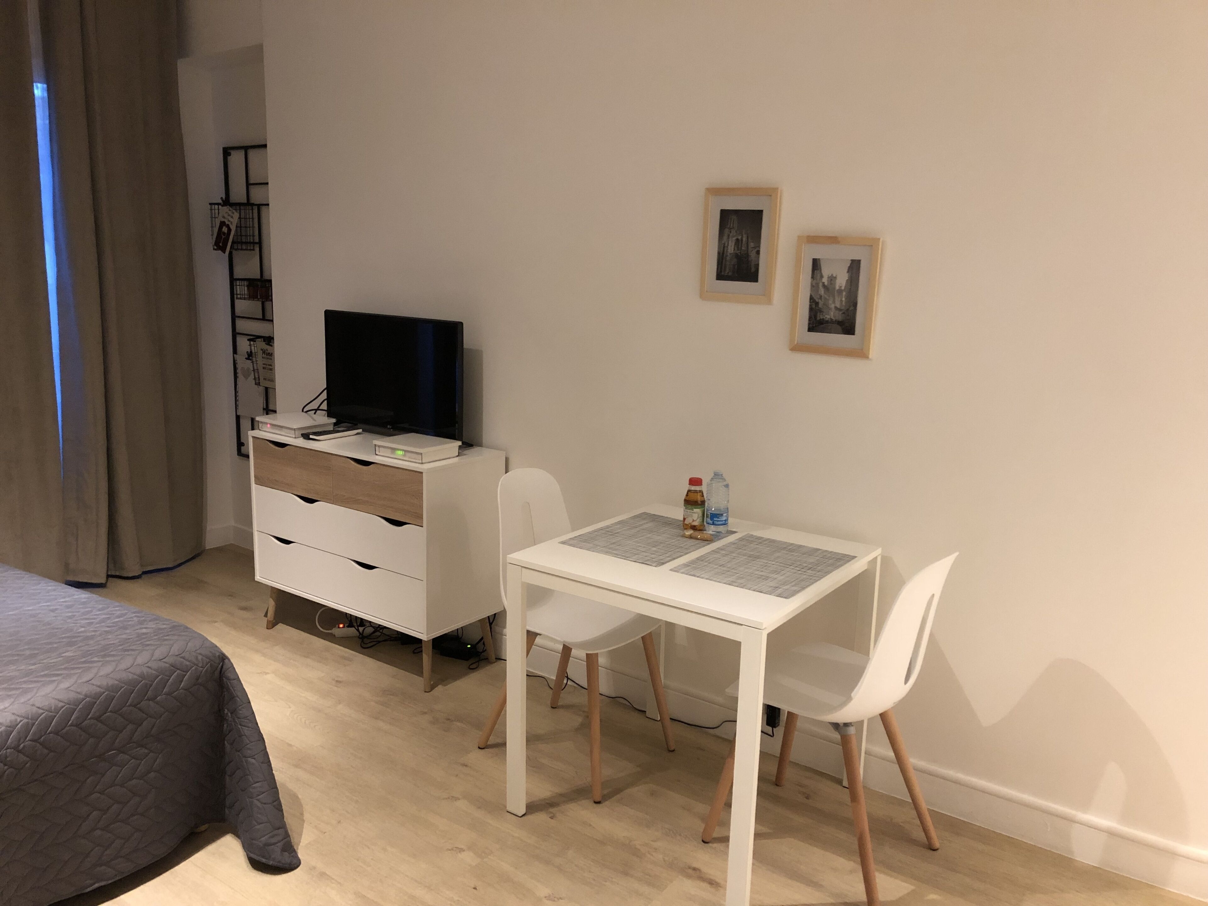 Un dormitorio con una cama, un escritorio con computadora, un televisor y dos cuadros en la pared.