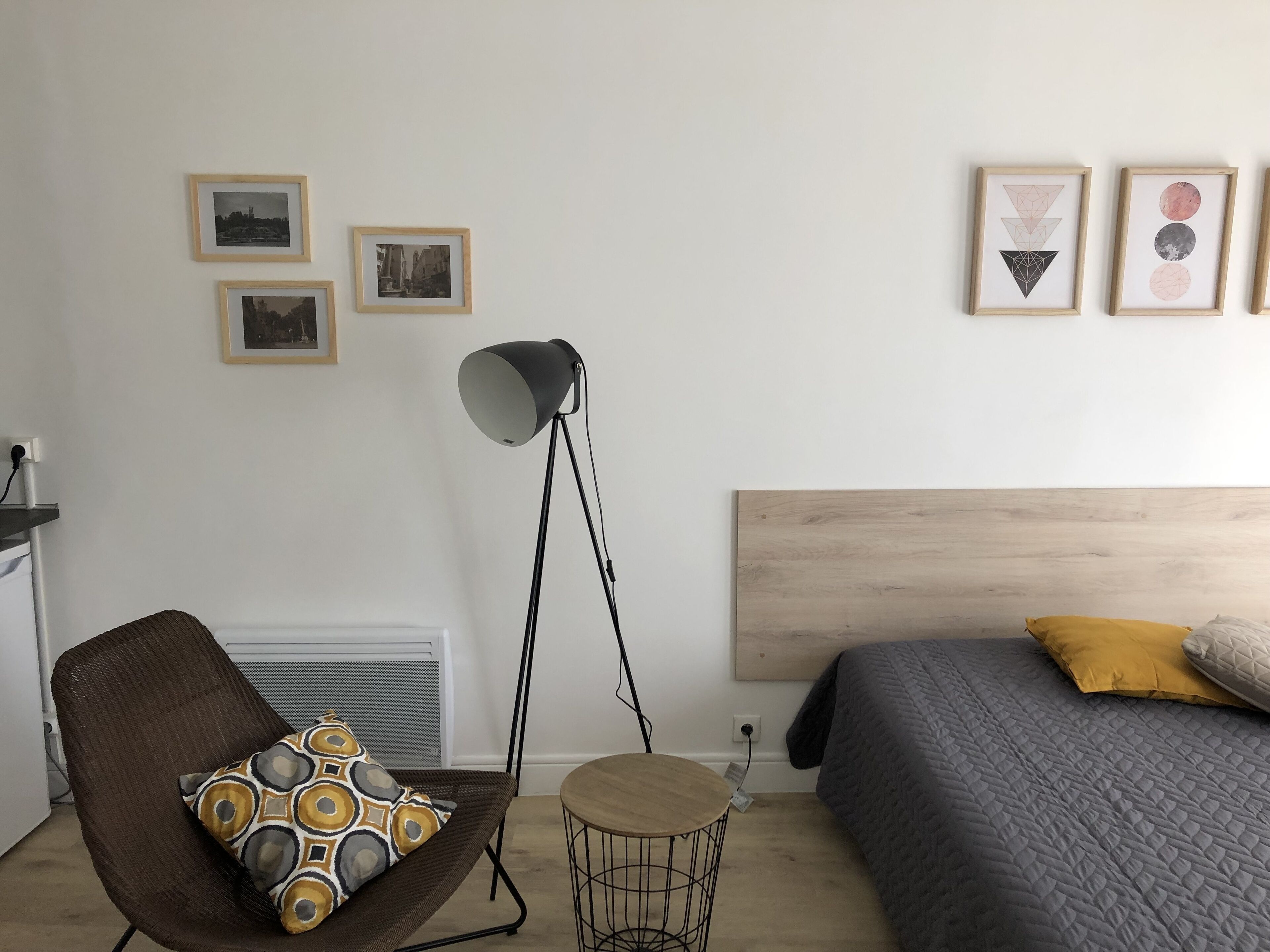 A bedroom with a bed, a chair, a floor lamp, and wall art.