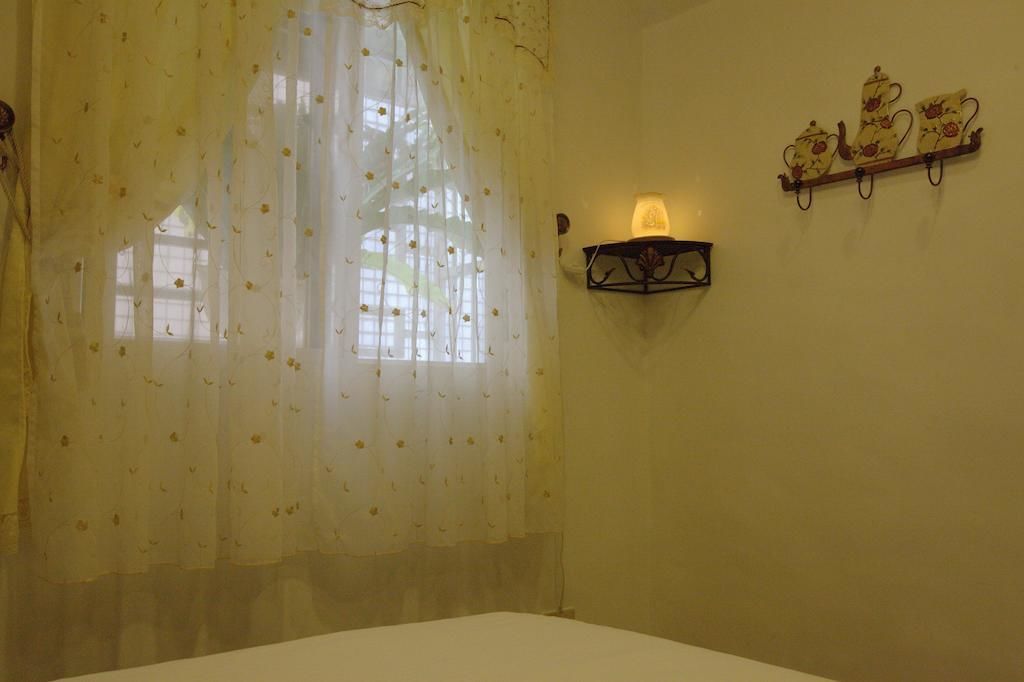 Ein Zimmer mit einem Bett, einem Fenster mit durchsichtigen Vorhängen und einer Wandregal mit Dekoration.