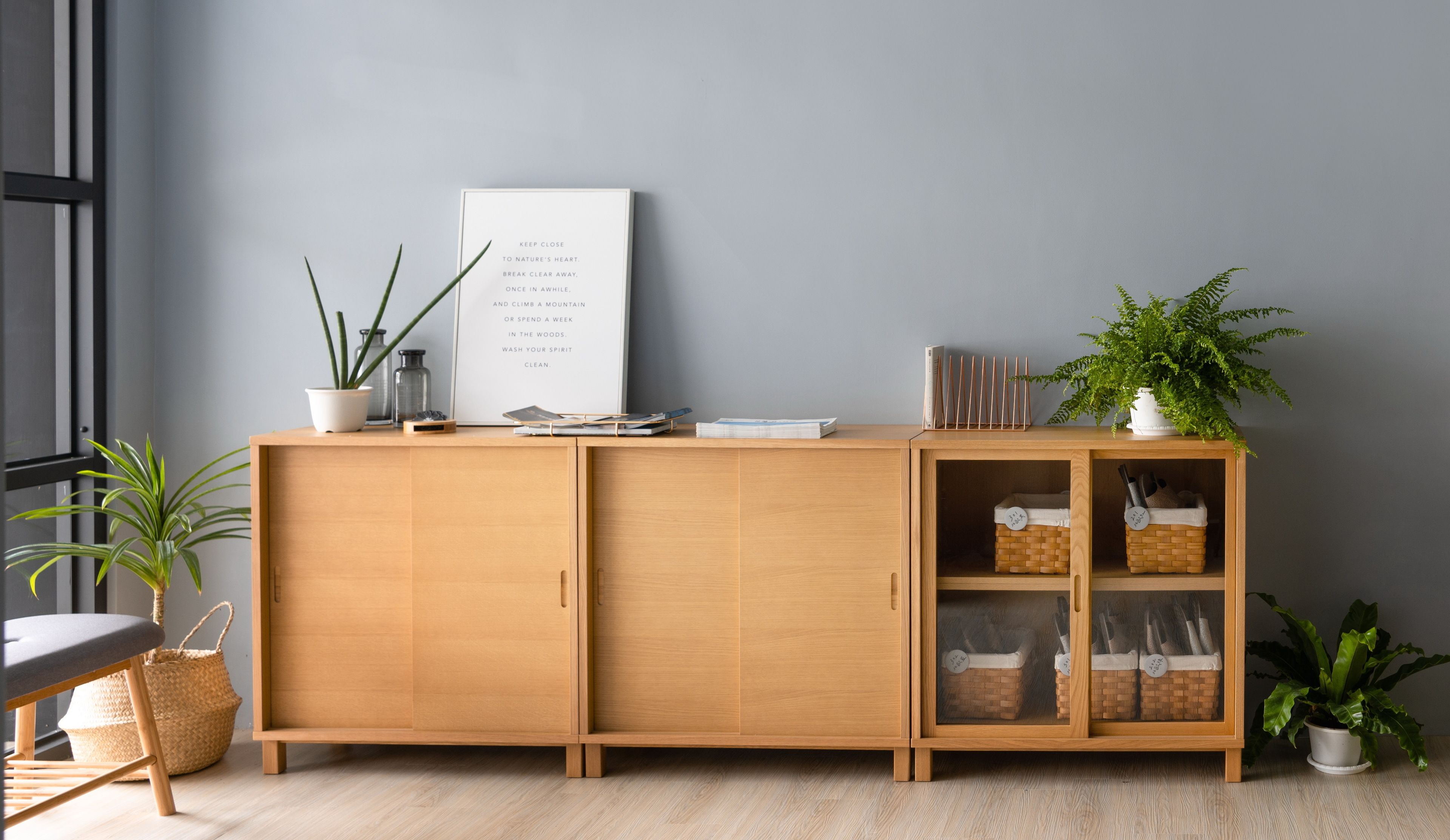 A wooden cabinet with open shelves, a framed inspirational quote, and potted plants.