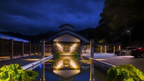 A nighttime view of a building with a reflective water feature in the foreground, a red car parked on the right, and a clear sky. - Fugaku Gunjo (Izu)