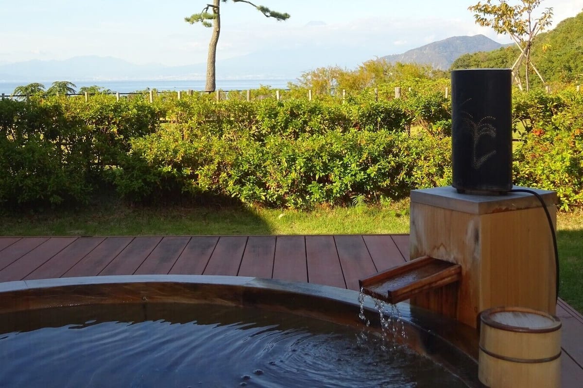 Un jacuzzi con caída de agua, rodeado por una terraza de madera y un seto.