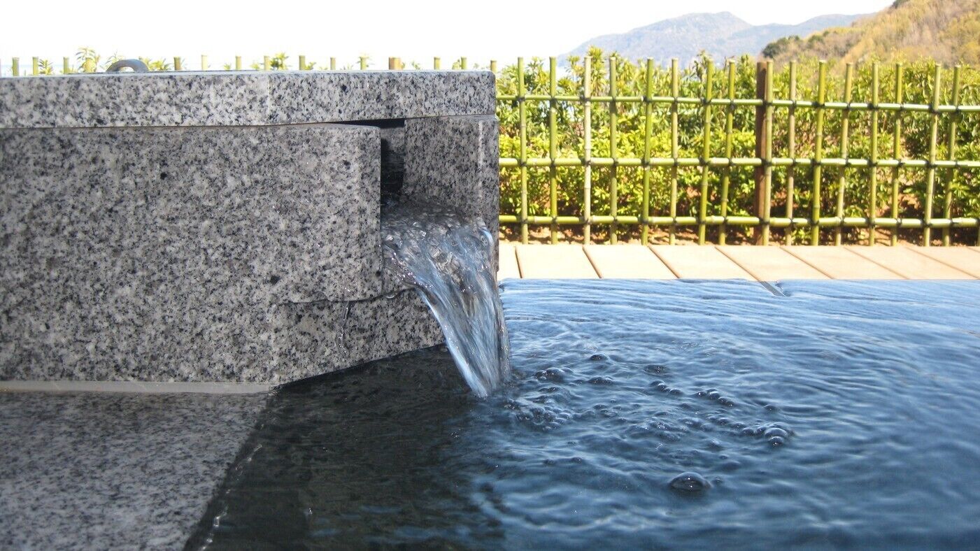 A water feature with a granite structure and a bamboo fence in the background.