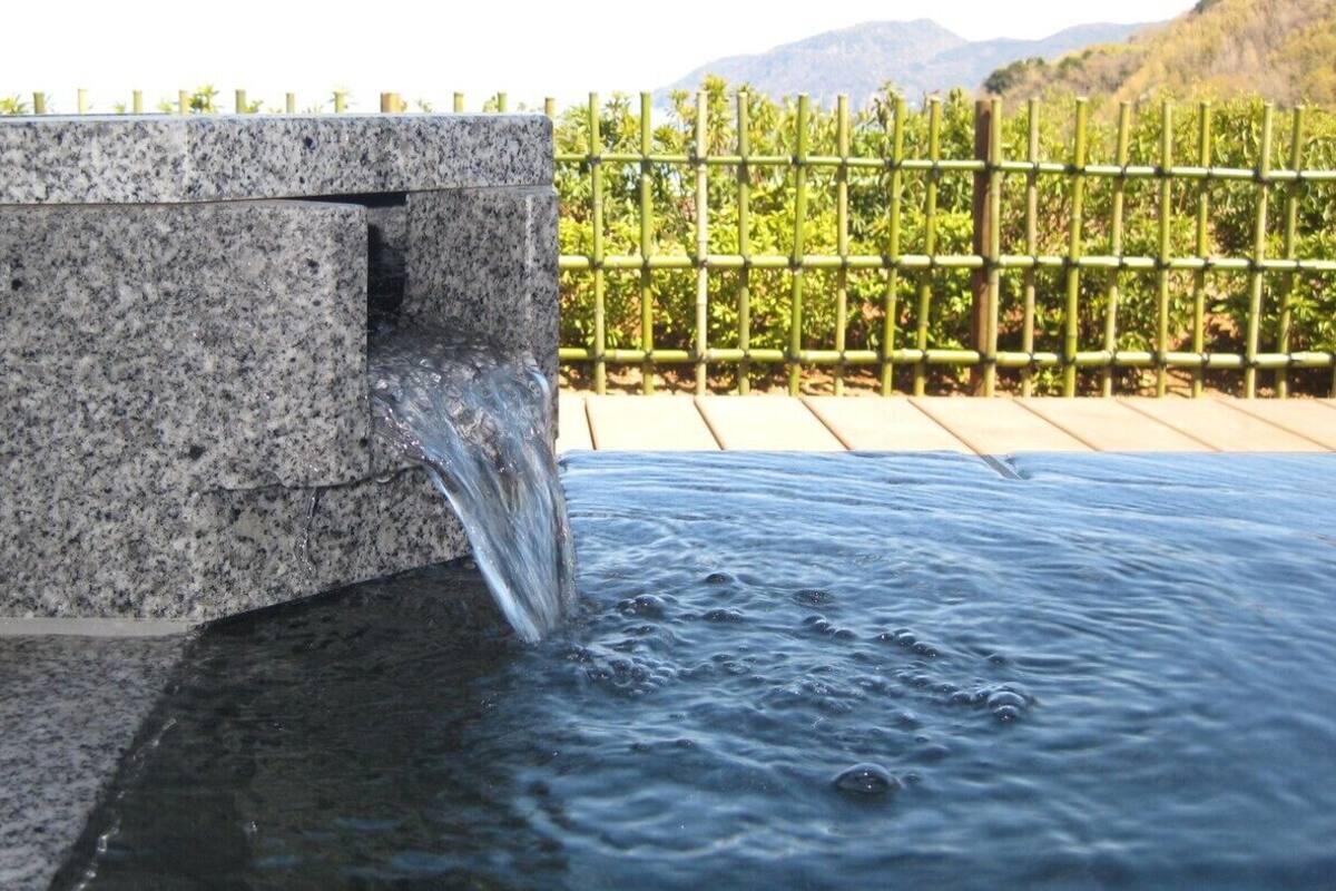Una fuente de agua con una estructura de granito y una valla de bambú al fondo.