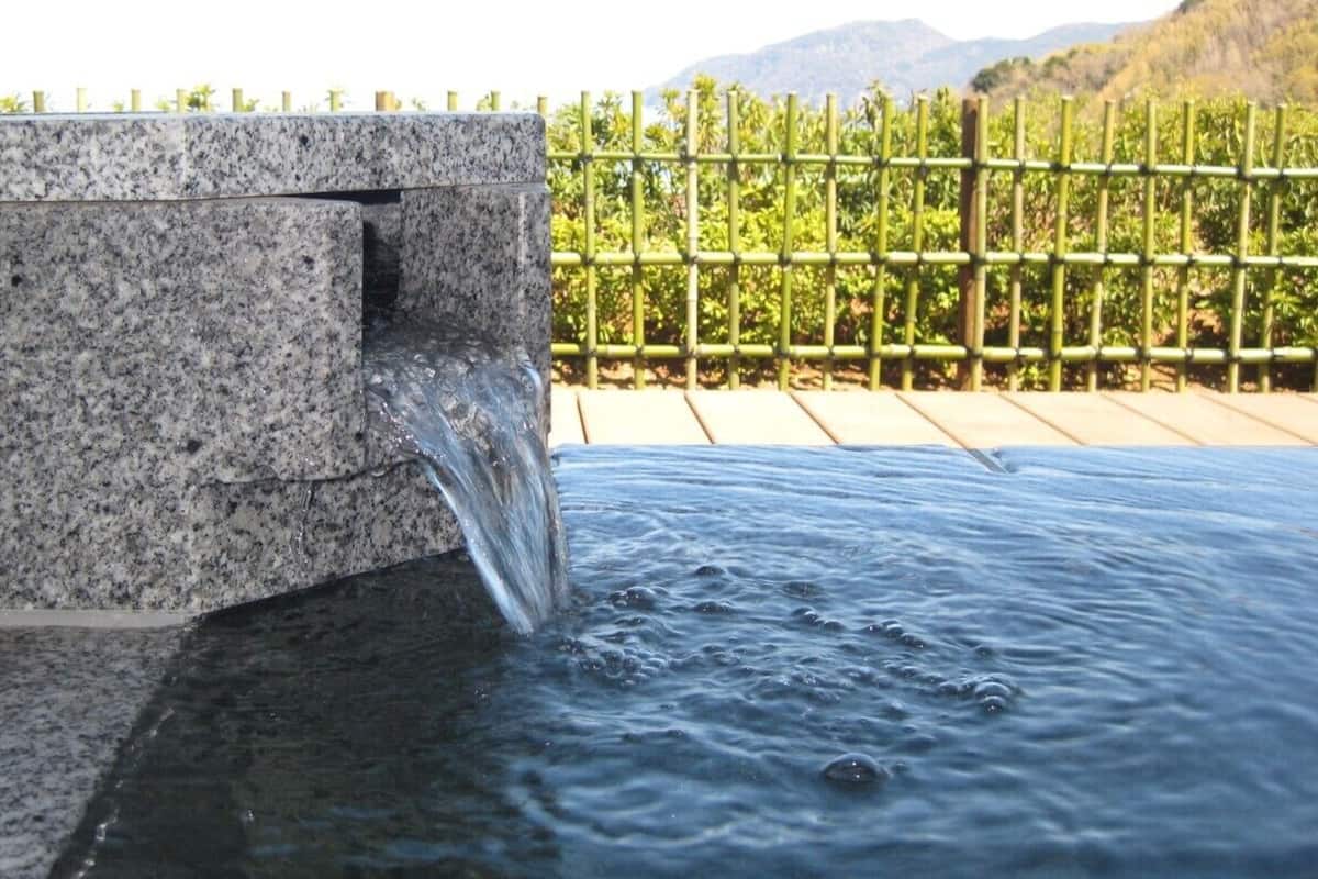 Uma fonte com estrutura de granito e cerca de bambu ao fundo.