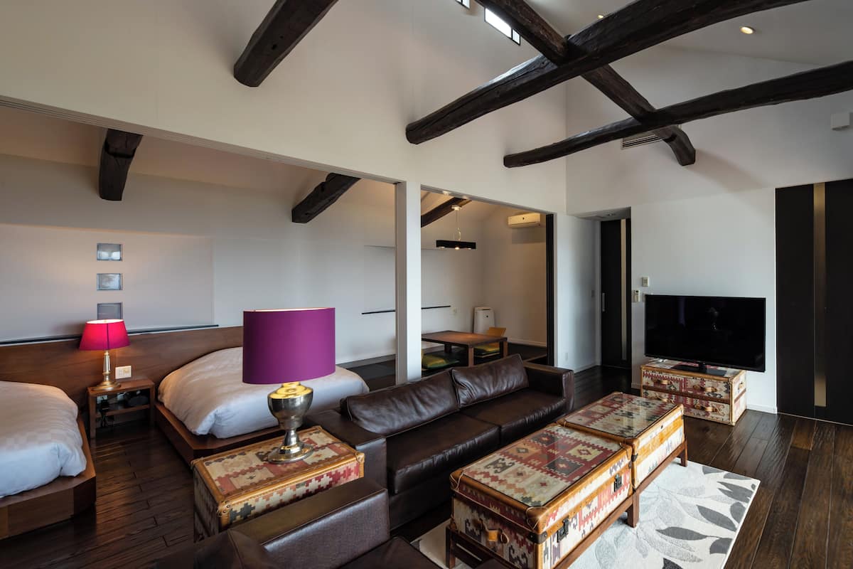 Una habitación de hotel moderna con una cama grande, un sofá de cuero, un televisor y techo de madera.