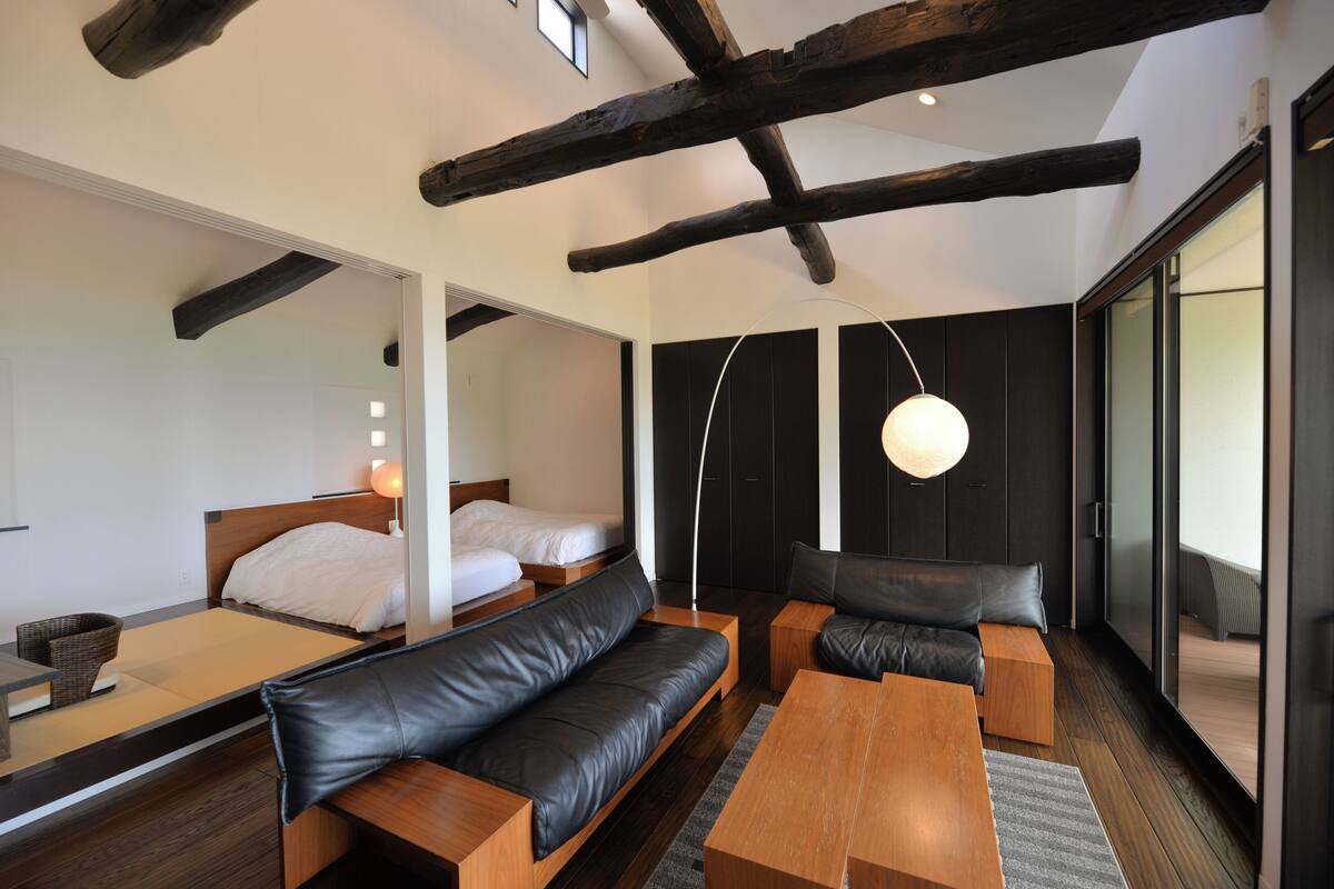 Una habitación de hotel moderna con techo de madera, sofá, cama y un ventanal grande.