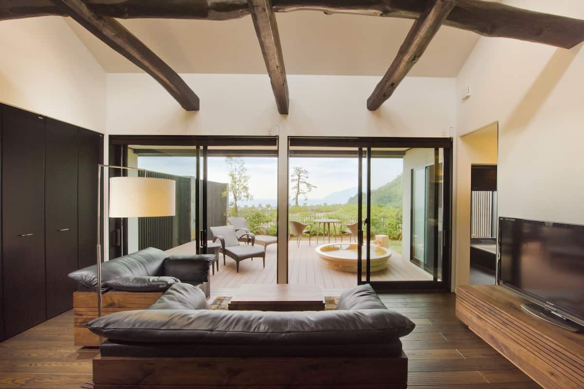 Una sala de estar moderna con un sofá, una mesa de centro y un televisor. Hay un balcón con una mesa y sillas, y vistas al exterior.
