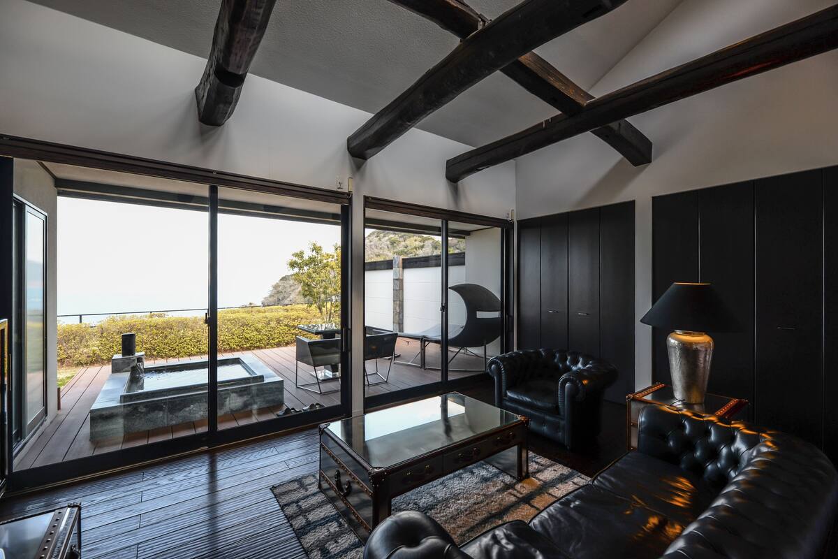Una sala de estar moderna con una mesa de centro de vidrio, sofá de cuero y vistas a una terraza con mobiliario exterior.